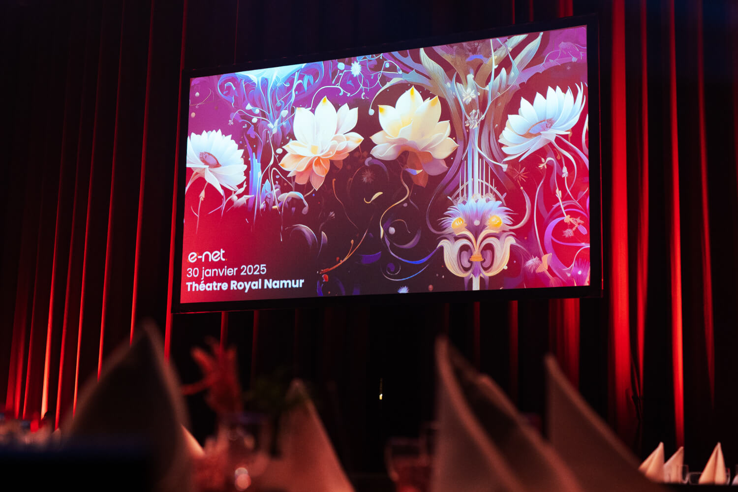 Grande télévision en face des rideaux rouges du théâtre projetant des ornements floraux ainsi que la date 30 Janvier 2025.
