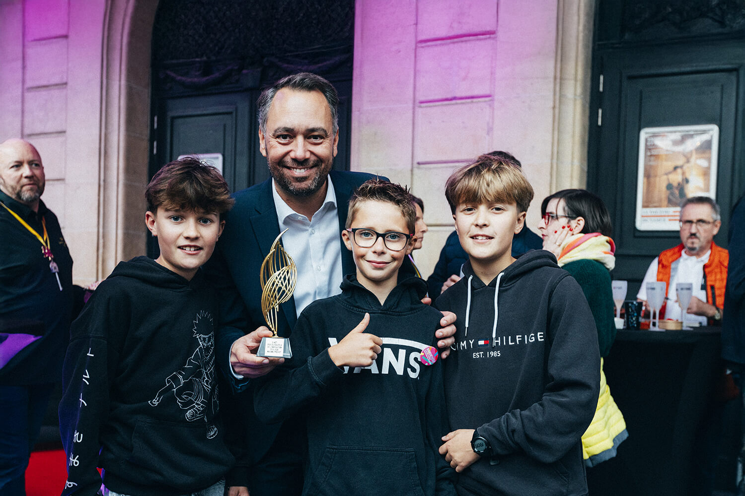  Maxime Prévot, lauréat du Souffle de l'innovation, entouré de 3 jeunes adolescents, brandissant fièrement son trophée.