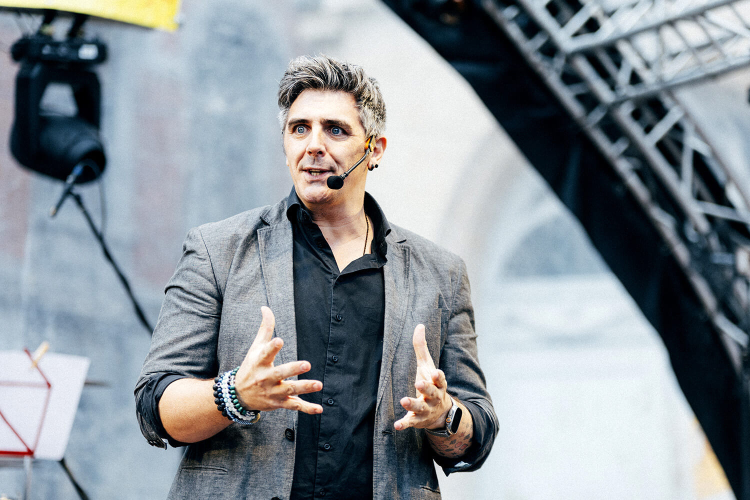 Benjamin Ghislain, mentaliste, s'adresse au public lors d'une démonstration de magie cognitive. Il utilise des gestes pour illustrer ses propos, captivant l'audience avec son charisme.