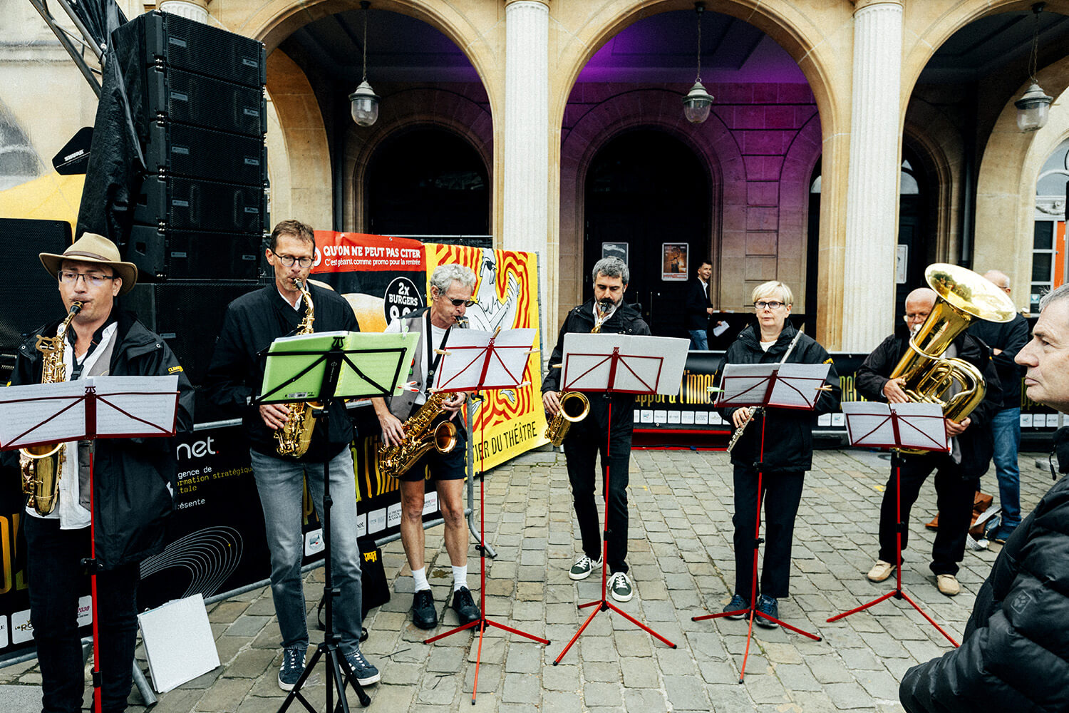 Les membres de la fanfare d’Assesse jouent ensemble sous une structure architecturale élégante. Chaque musicien, concentré sur sa partition.