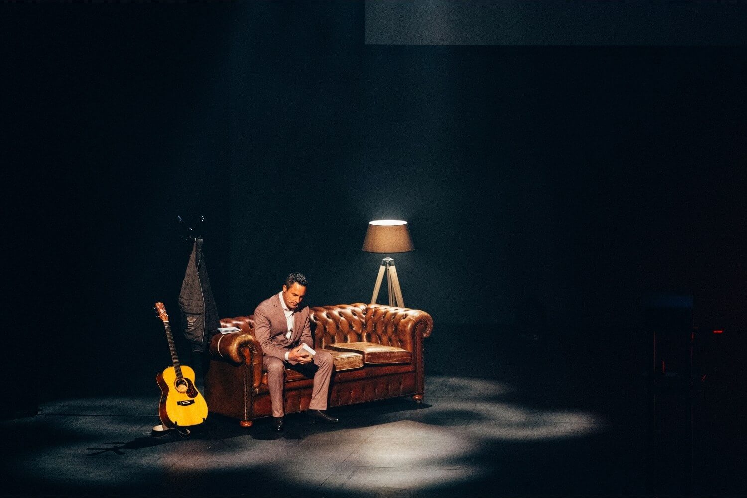 Nicolas Pourbaix assis seul sur un canapé sur scène, plongé dans une atmosphère feutrée, symbolisant le temps de l’introspection avant le lancement de l’expérience immersive de l’appel à l’innovation.