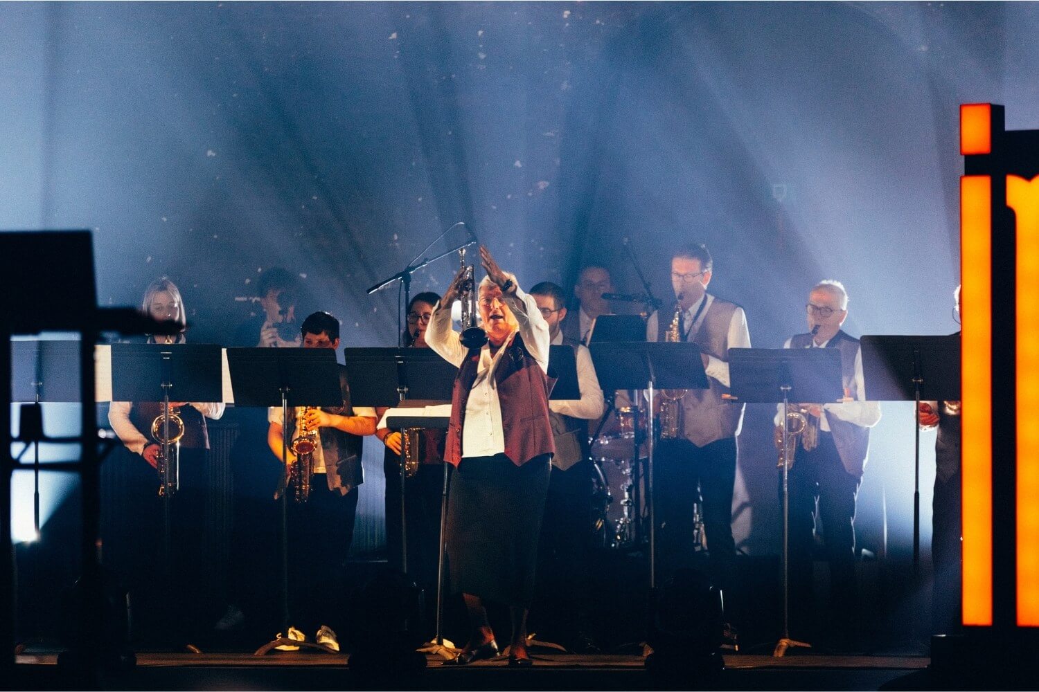 La cheffe de la fanfare Sainte-Cécile d’Assesse dirige les musiciens sur scène, symbolisant le rôle essentiel du pilotage, du cadre et de l’intention humaine.